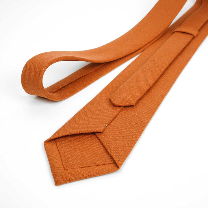 A zoomed-in view of the back of a burnt orange linen necktie, highlighting the textured weave and quality construction on a white background.