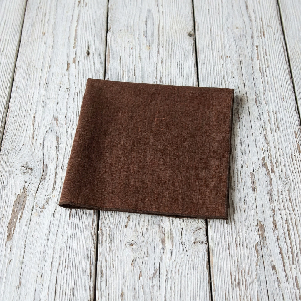 A Hemmitie brown linen fabric pocket square displayed on a rustic wooden surface.