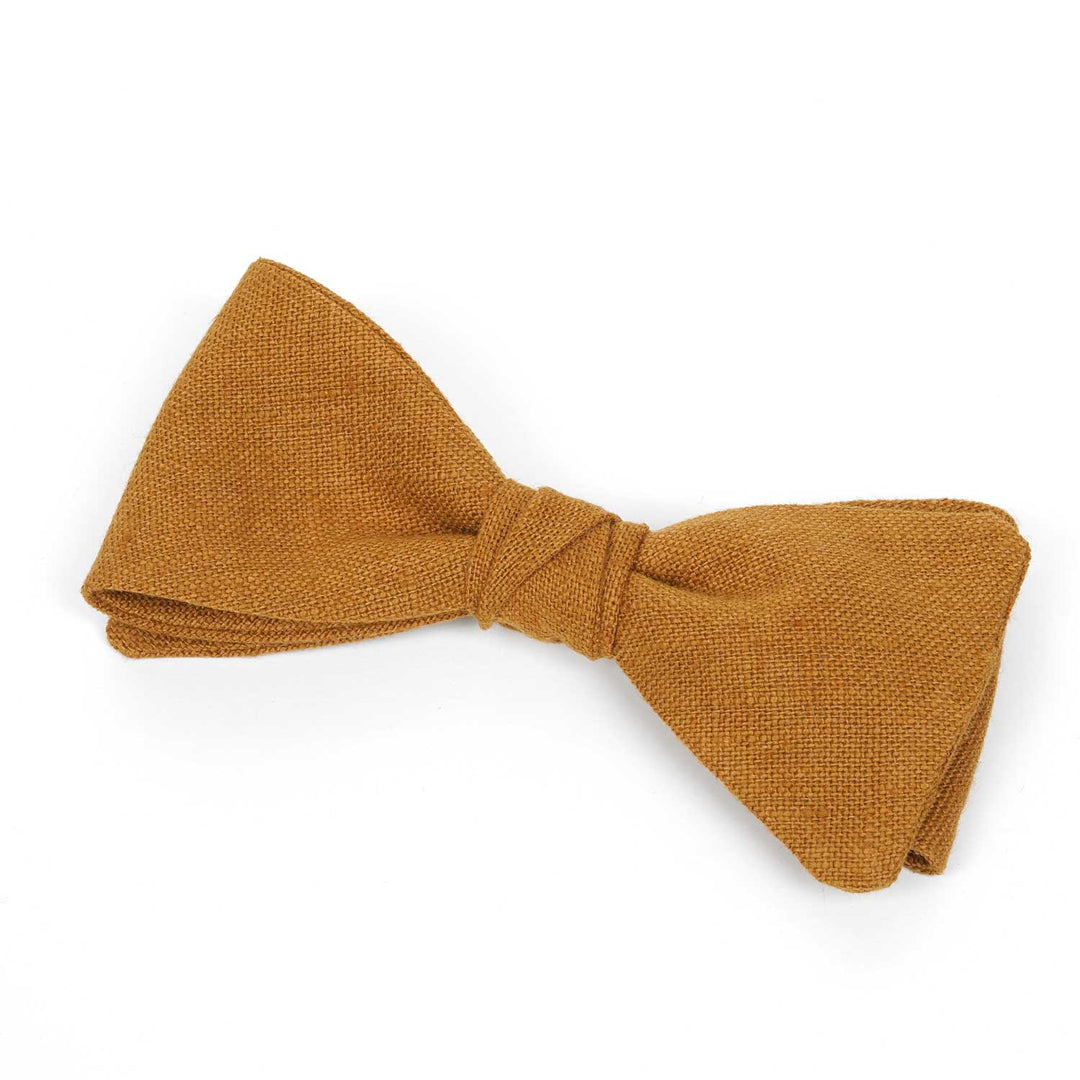 Side view detail of a Hemmitie cinnamon yellow linen pre-tied bow tie showing the textured fabric weave.