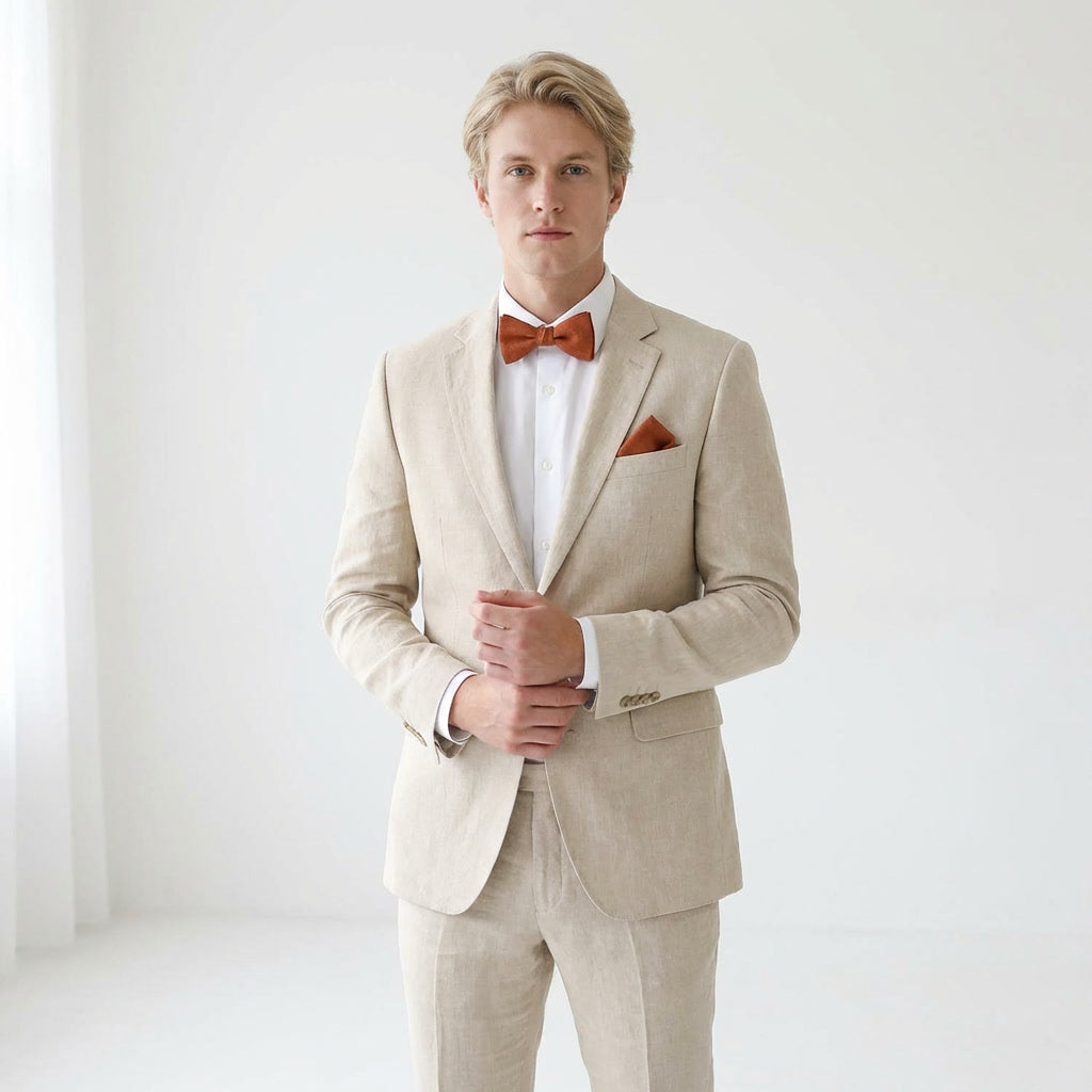 Man wearing a Hemmitie terracotta linen bow tie and matching pocket square with a beige linen suit on a white background.