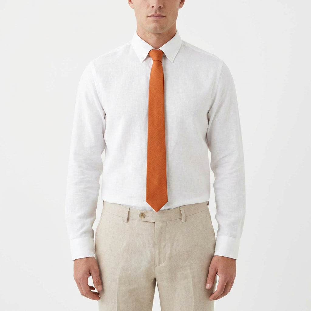 A man wearing a burnt orange linen necktie with a crisp white dress shirt and beige trousers, showcased on a clean white background.