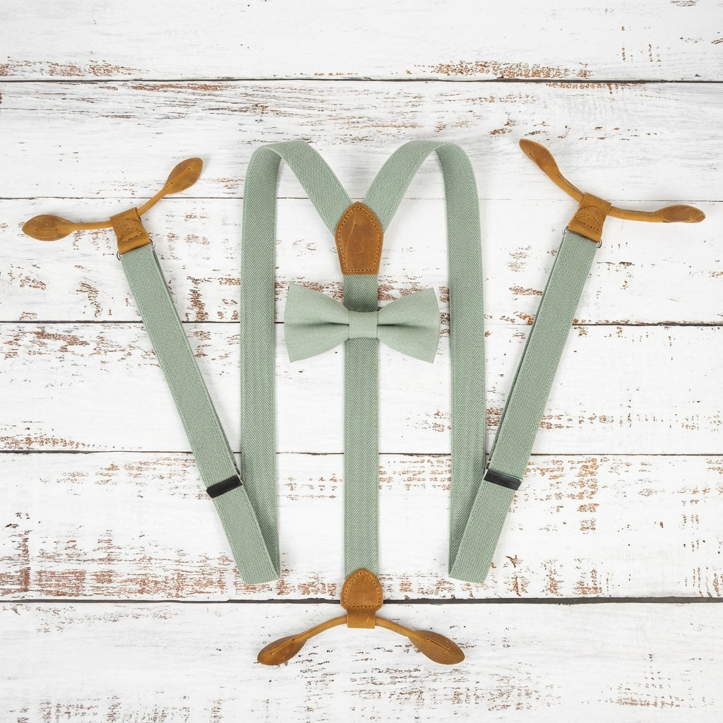 Top view of sage green button suspenders on a light wood background