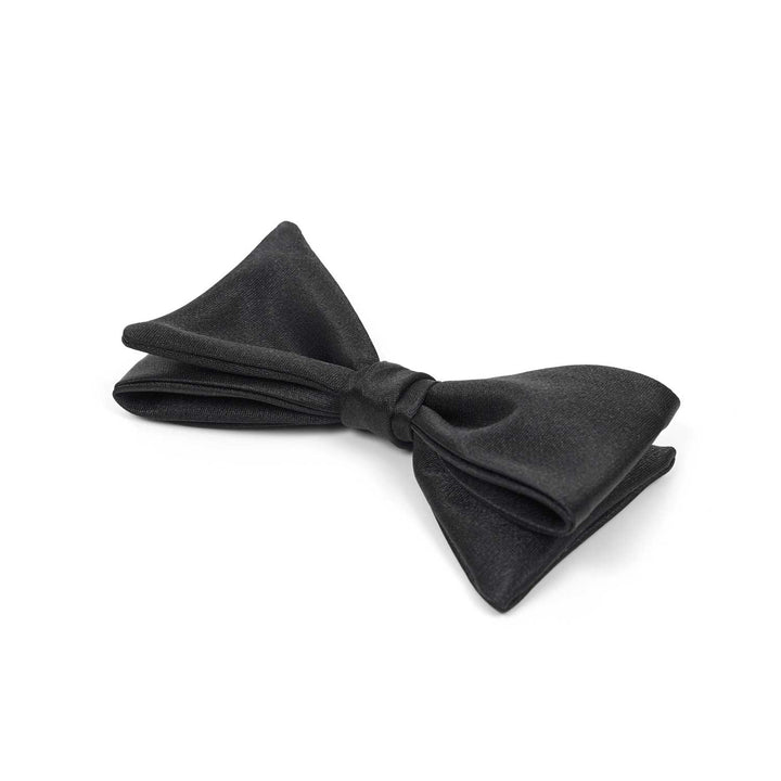 Close-up sideways view of a pre-tied black satin bow tie against a white background, showing the knot detail and fabric texture.